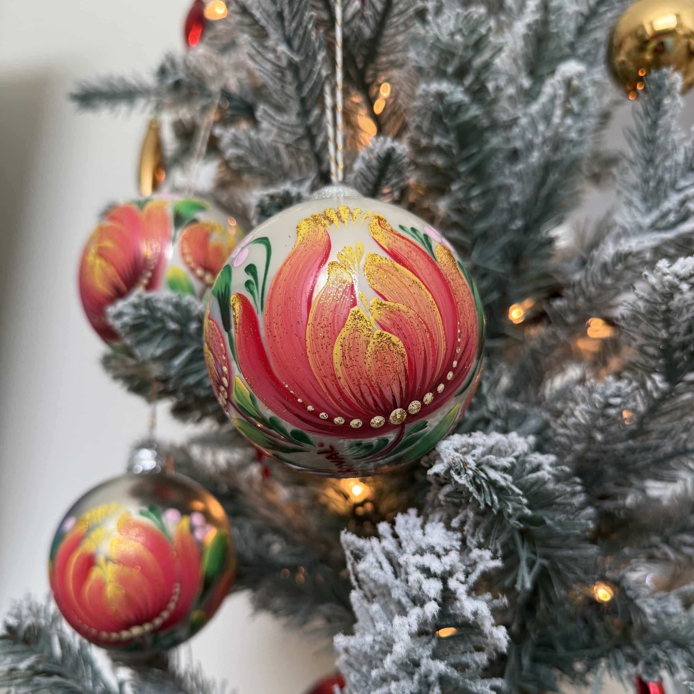 Hand-painted Christmas tree ornament featuring a pink floral design and gold glitter, 3-inch diameter